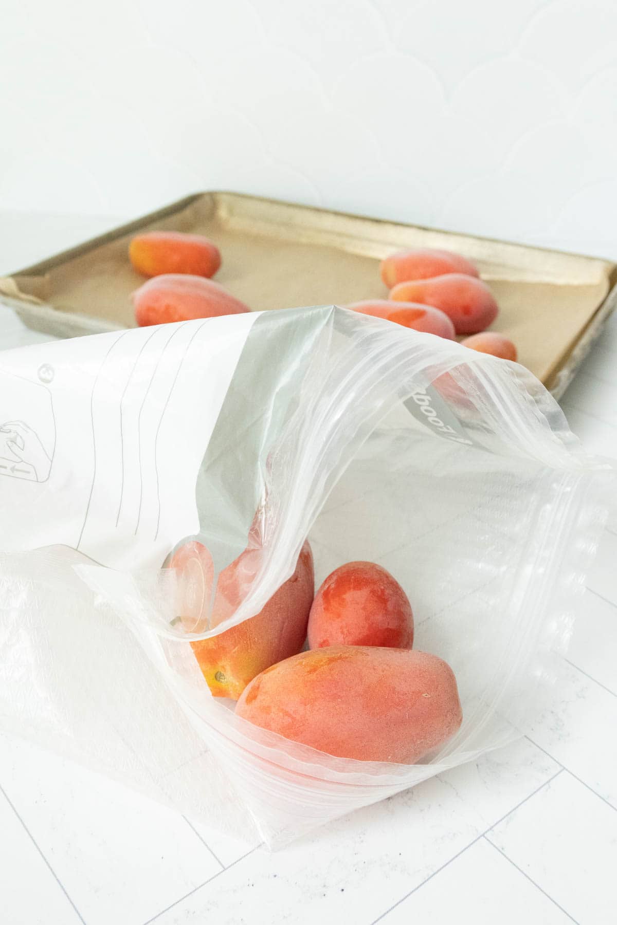 Frozen tomatoes in a plastic bag on top of a baking sheet.