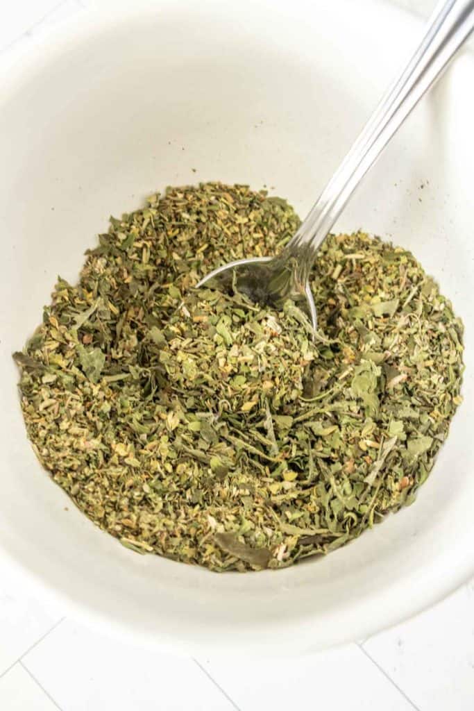 A spoonful of herbs in a white bowl.