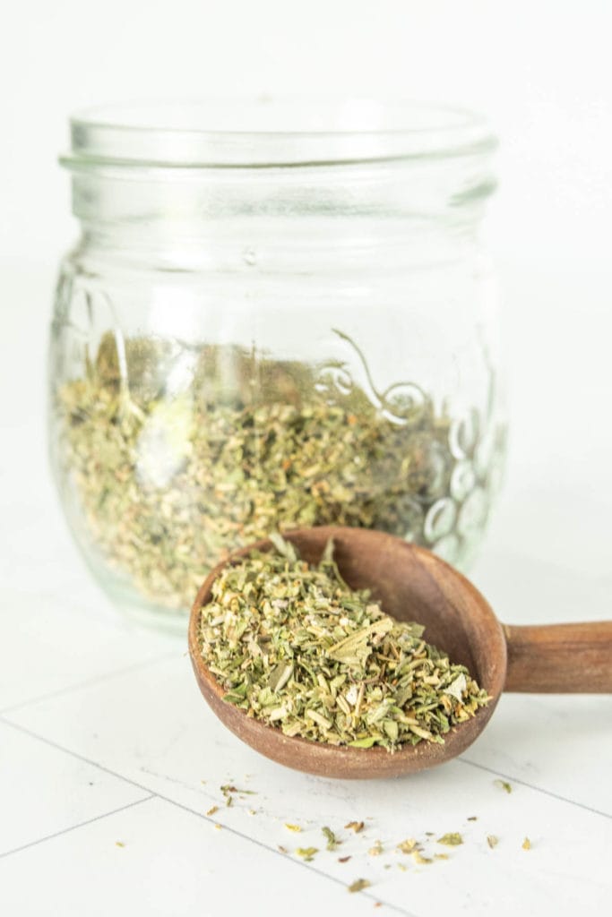 A wooden spoon filled with dried herbs in a glass jar.