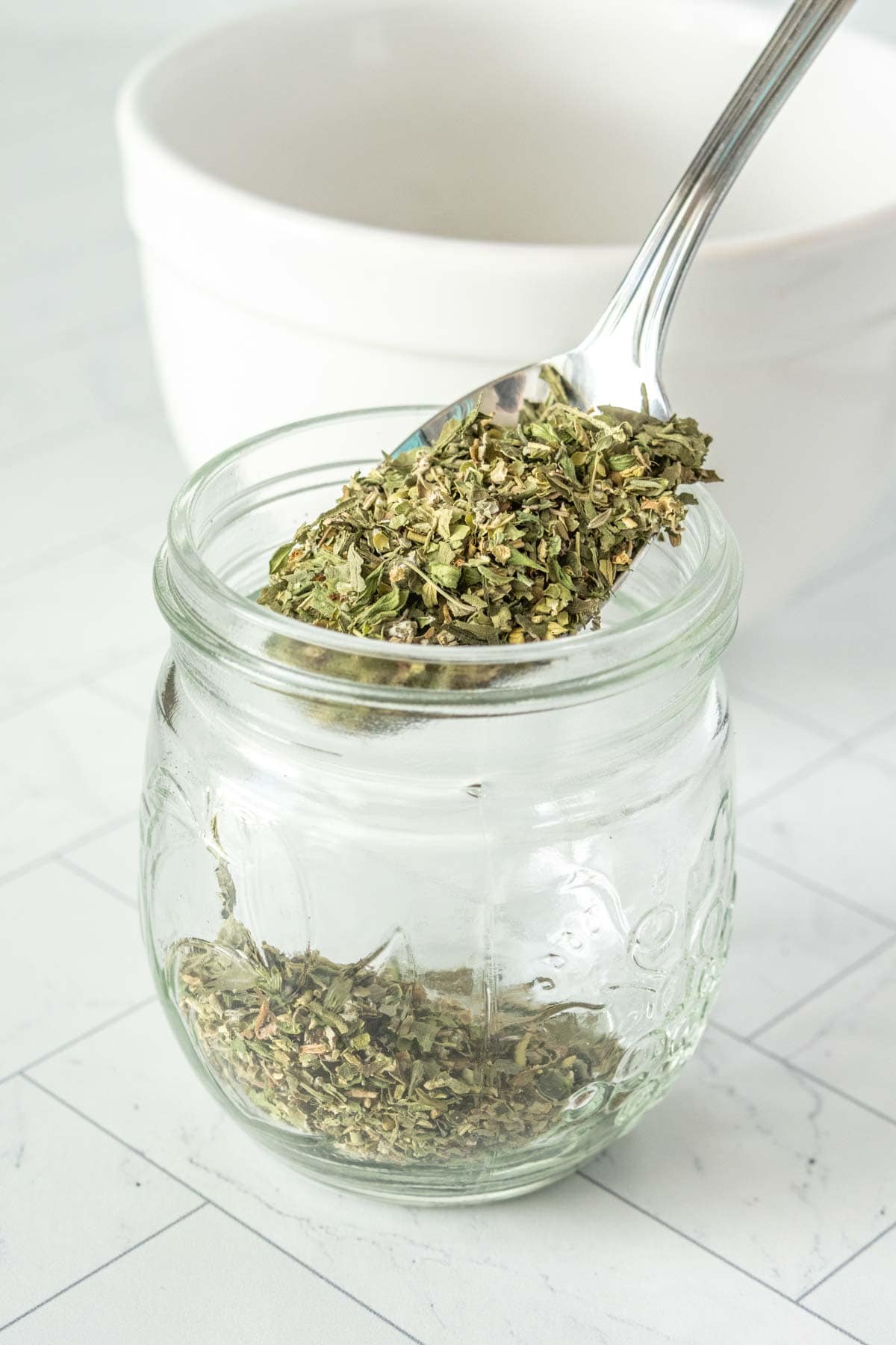 A spoonful of herbs in a glass jar.