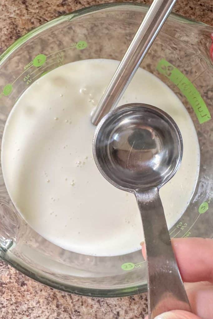 A person pouring clear extract into a glass bowl.