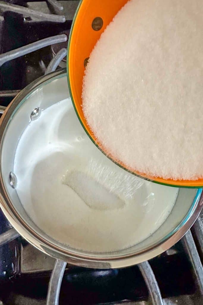 Sugar being poured into a pan on a stove.