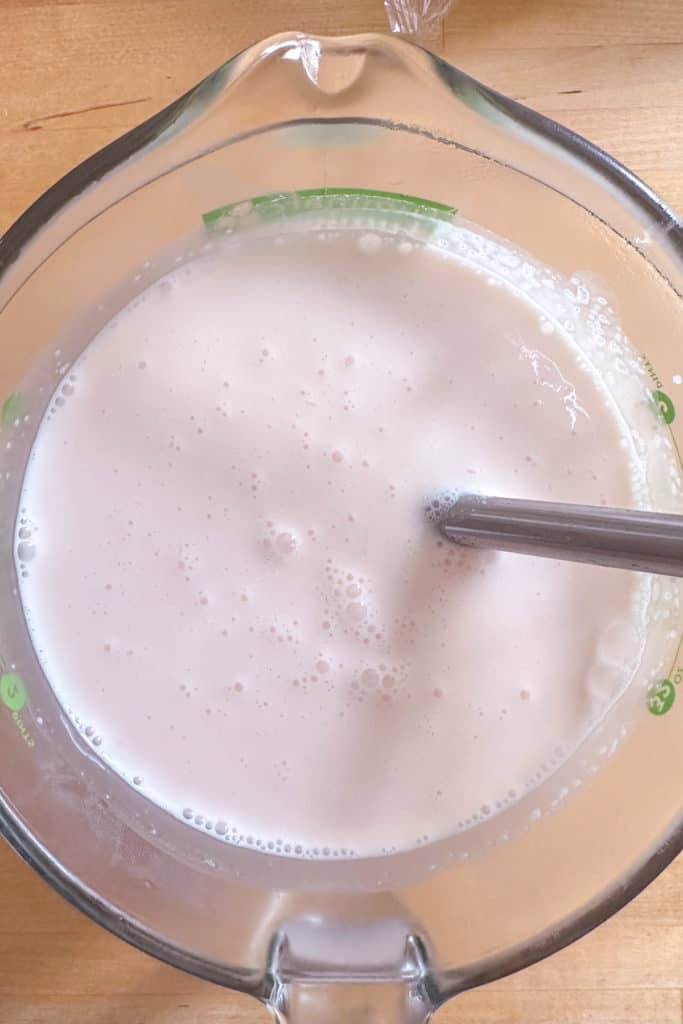 A glass bowl filled with ice cream base and a whisk.