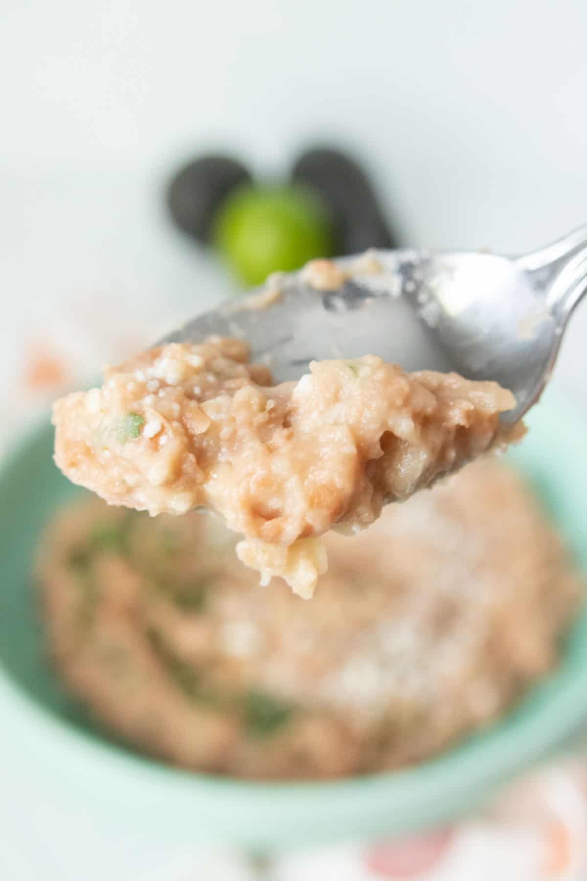 A spoon is holding a bite of refried beans.