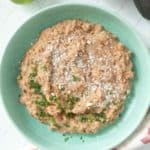 A bowl of refried beans on a table next to a lime.