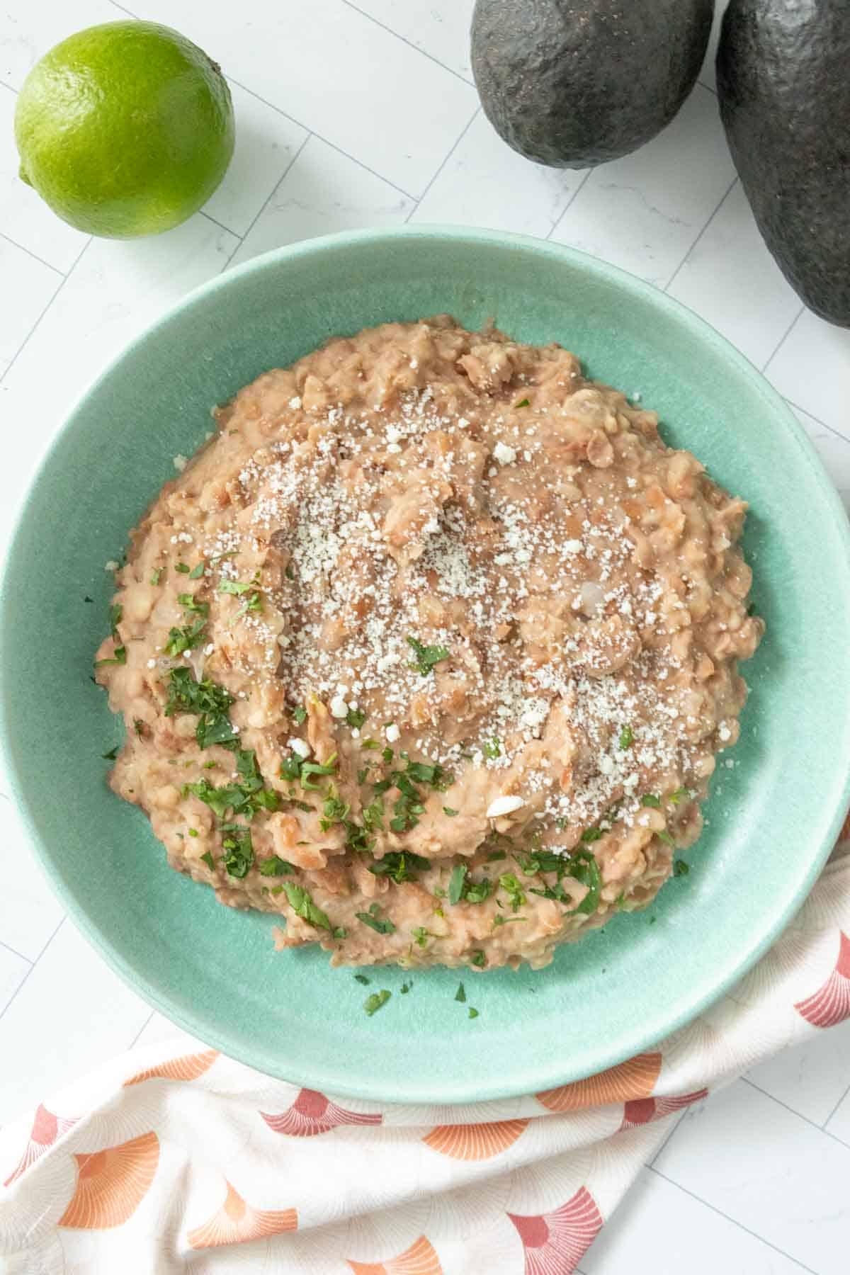 A bowl of refried beans on a table next to a lime.