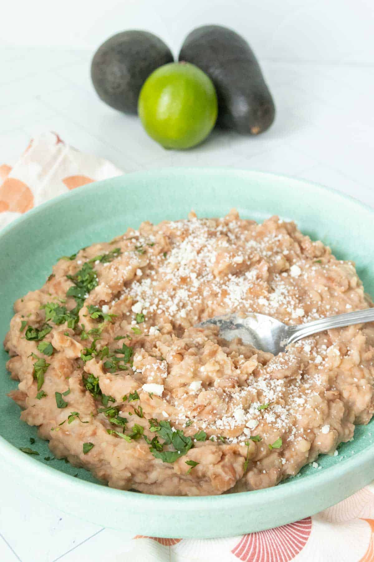 A bowl of refried beans with cilantro and cheese on a table.