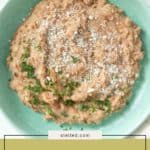 A plate of creamy refried beans garnished with chopped herbs and grated cheese, served on a vibrant green dish.