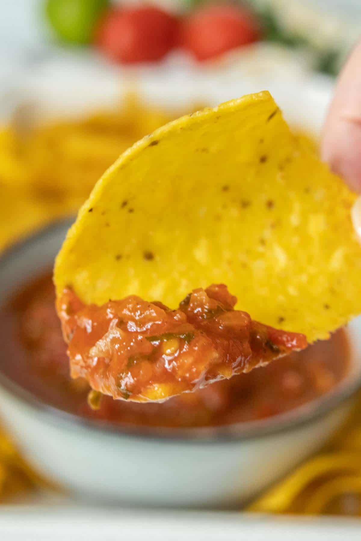 A person is dipping a tortilla into a bowl of salsa.