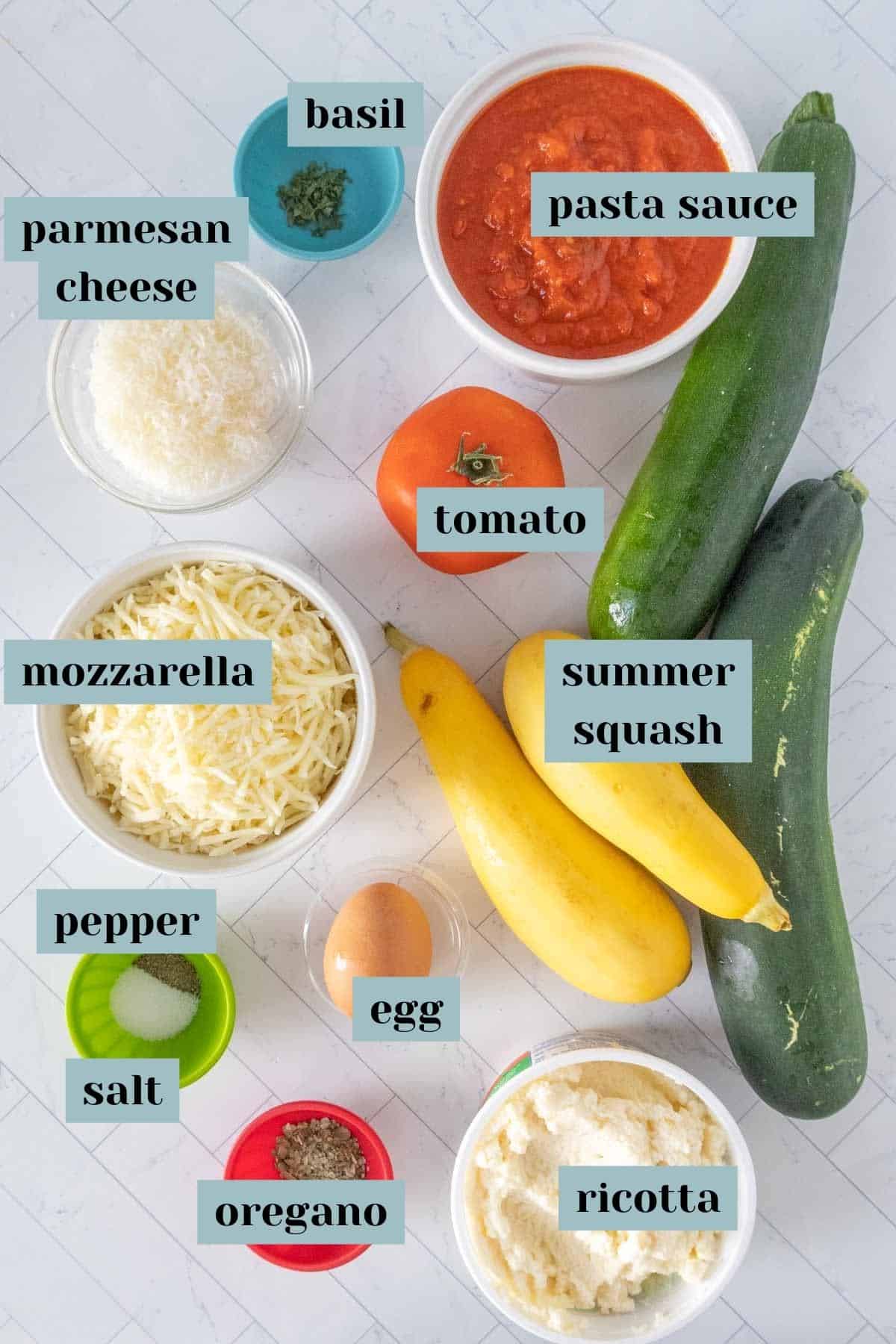 Ingredients for zucchini lasagna on a tile surface with labels.