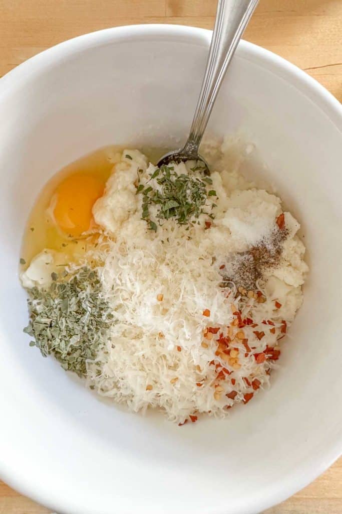 Ricotta, parmesan, egg, herbs, and spices in a white bowl before mixing.