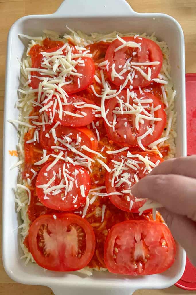 Sprinkling cheese on top of layered zucchini lasagna before baking.