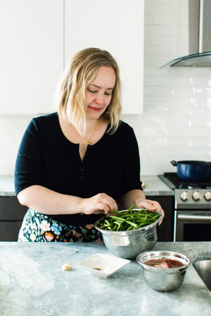 White woman picking string beans out of bowl.