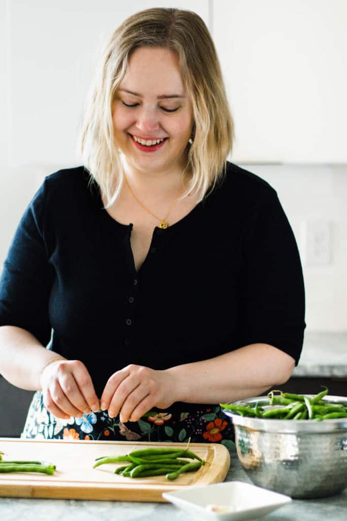 White woman in a black shirt snapping ends off string beans.