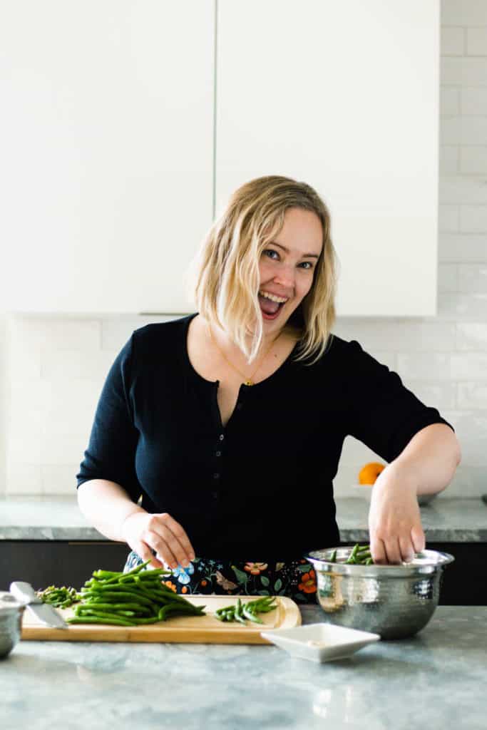White woman in a black shirt laughing while grabbing beans.