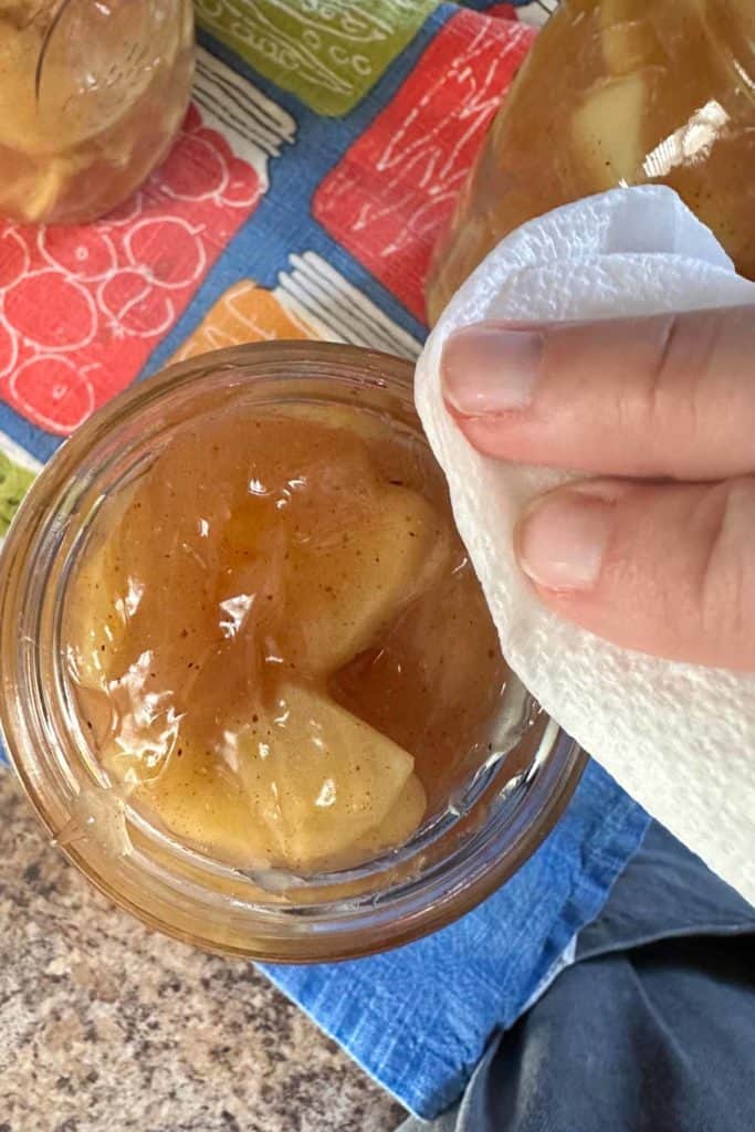 A person wiping a cloth over a jar of apple pie filling.