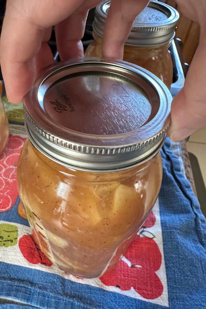 A person holding a jar of apple pie filling.