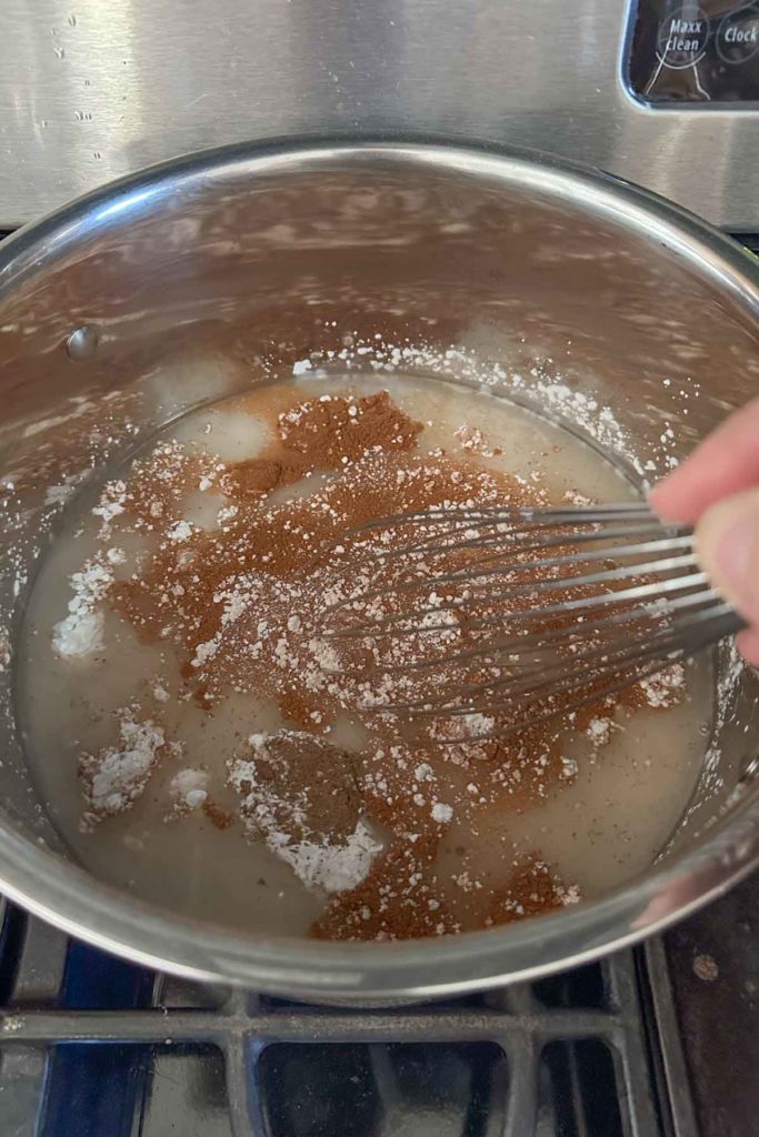 A person whisking sugar into a pan on a stove.