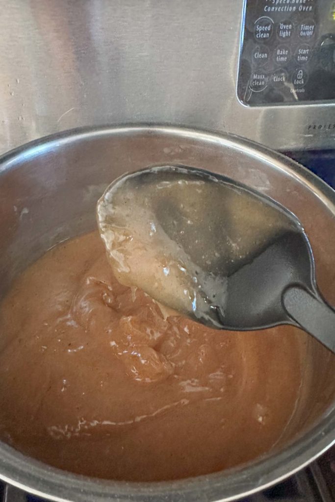A spoon is being used to stir a brown liquid in a pot.