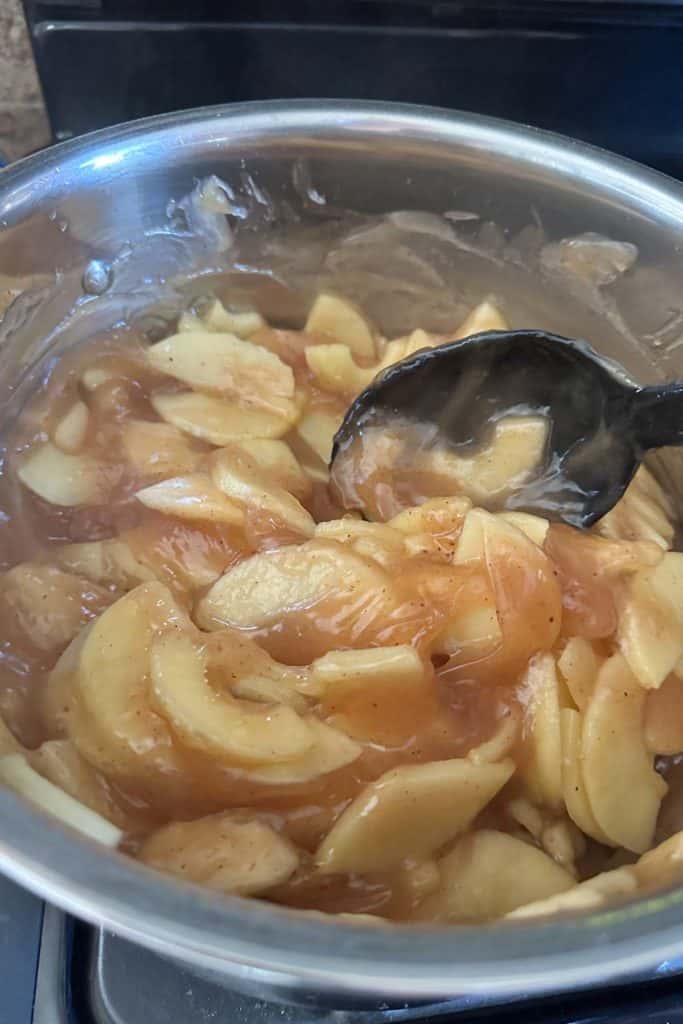 A bowl of apples in a sauce with a spoon.