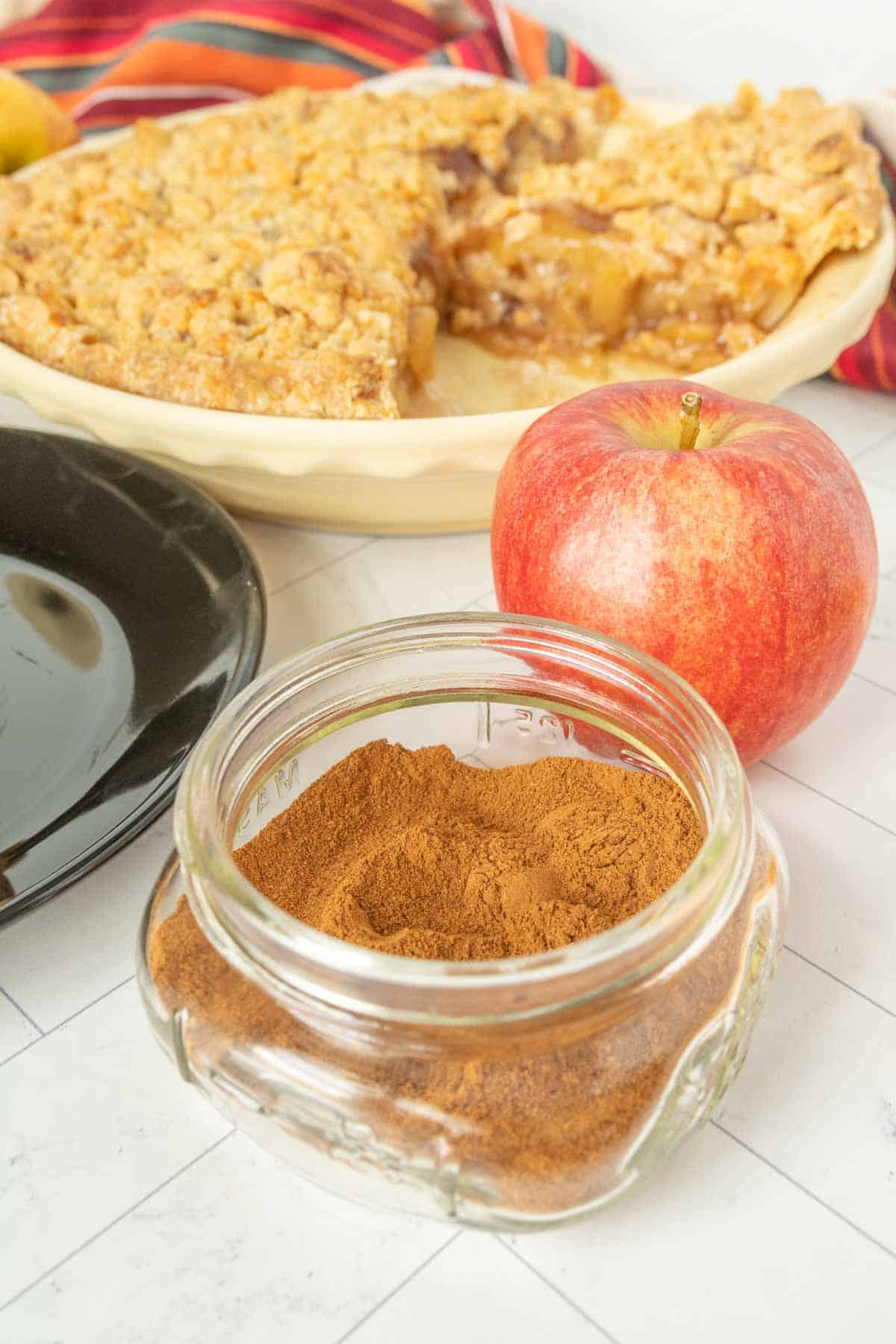 A bowl of apple pie spice next to a pie and a bowl of apples.