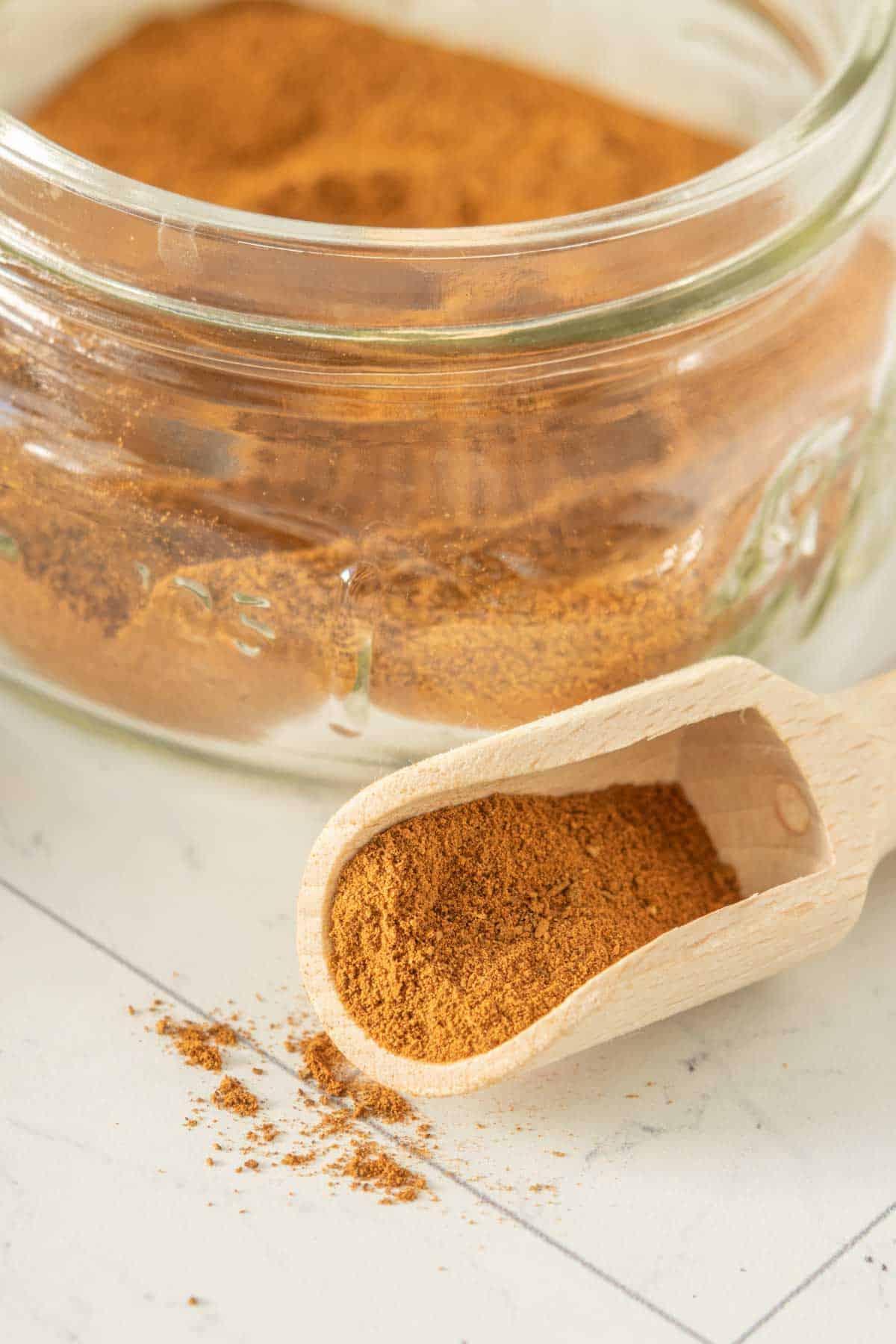 Apple pie spice in a glass jar with a wooden spoon.