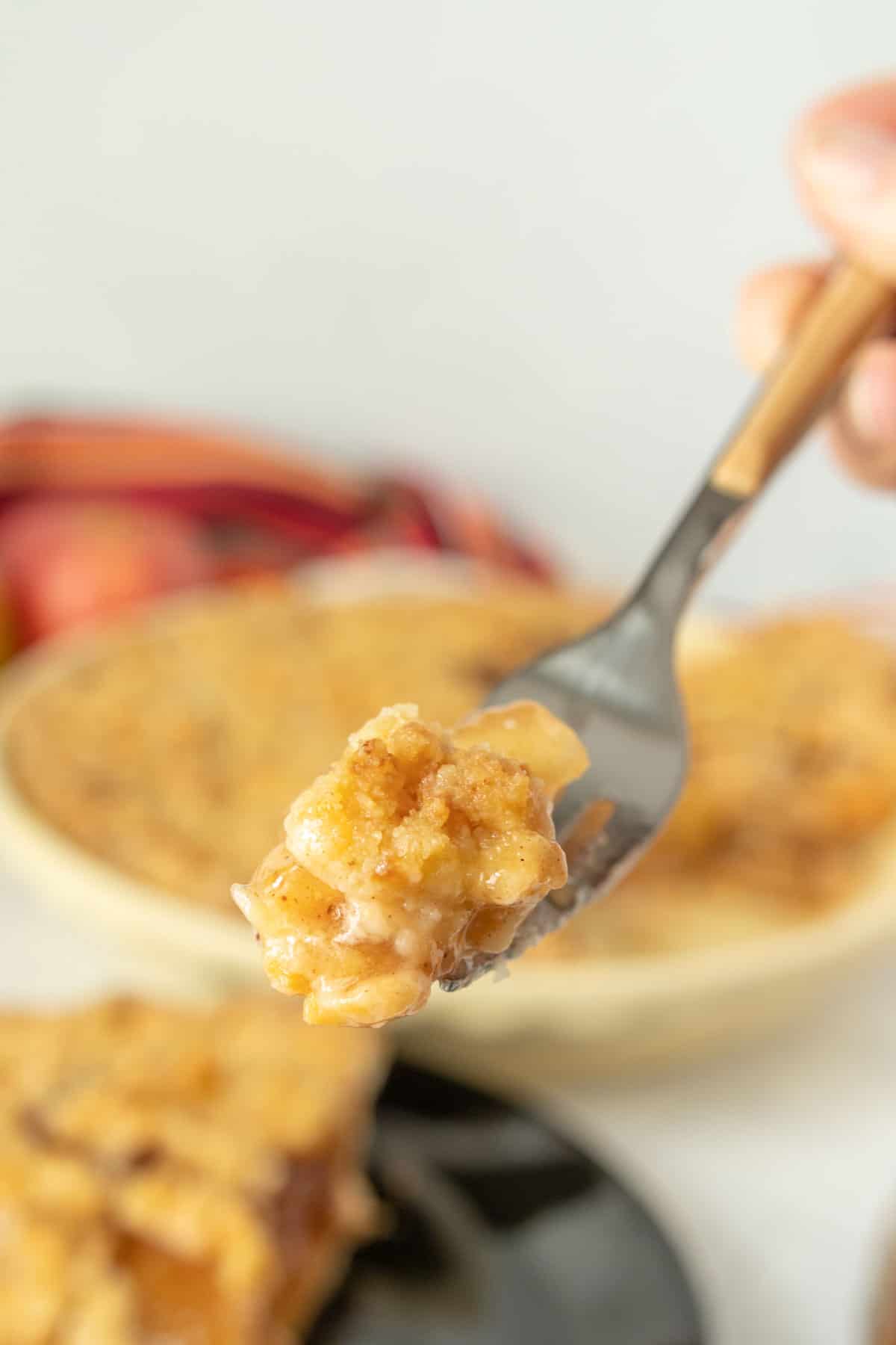 A person holding a piece of apple pie on a fork.