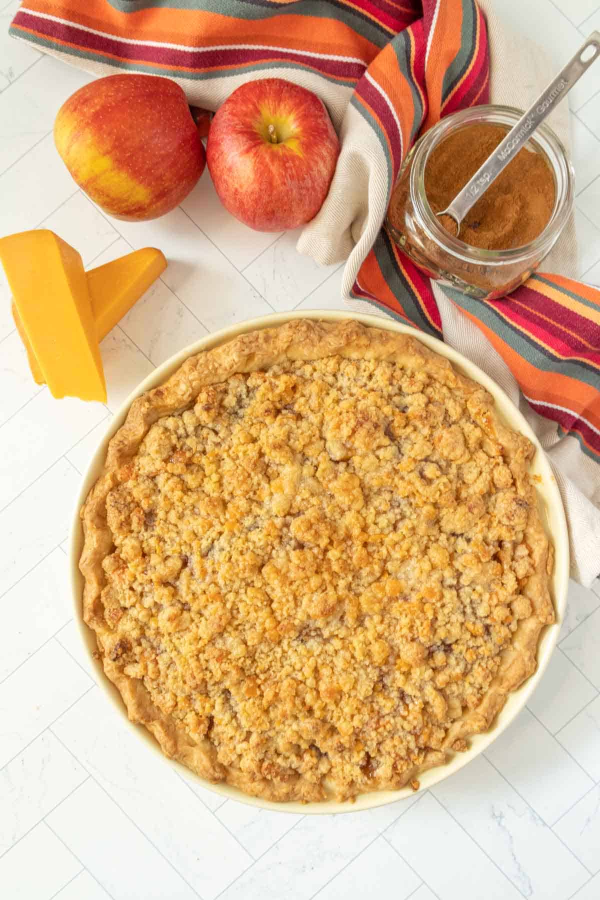 A pie is sitting on a table next to apples and cheese.