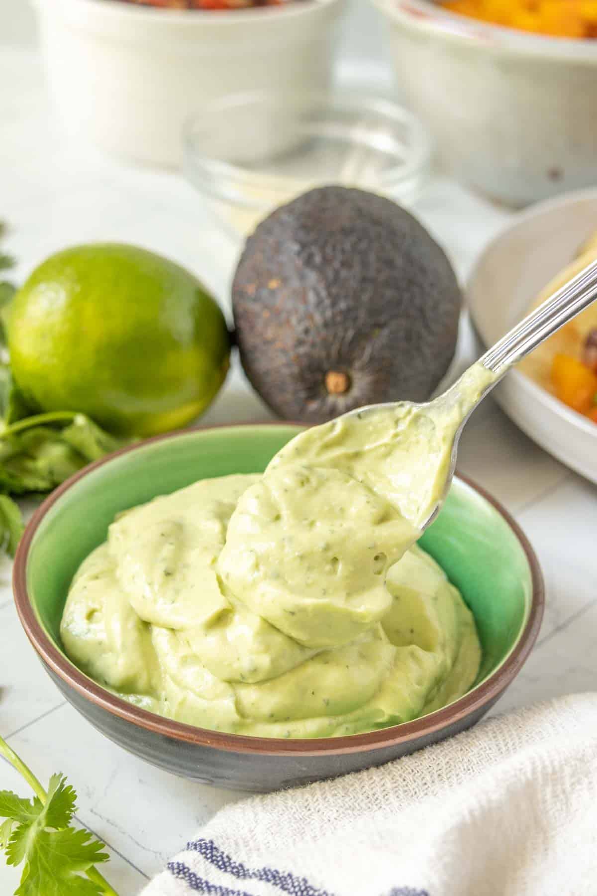 Avocado crema in a bowl with limes and cilantro.