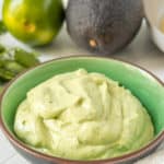 Avocado crema in a bowl with limes and other ingredients.