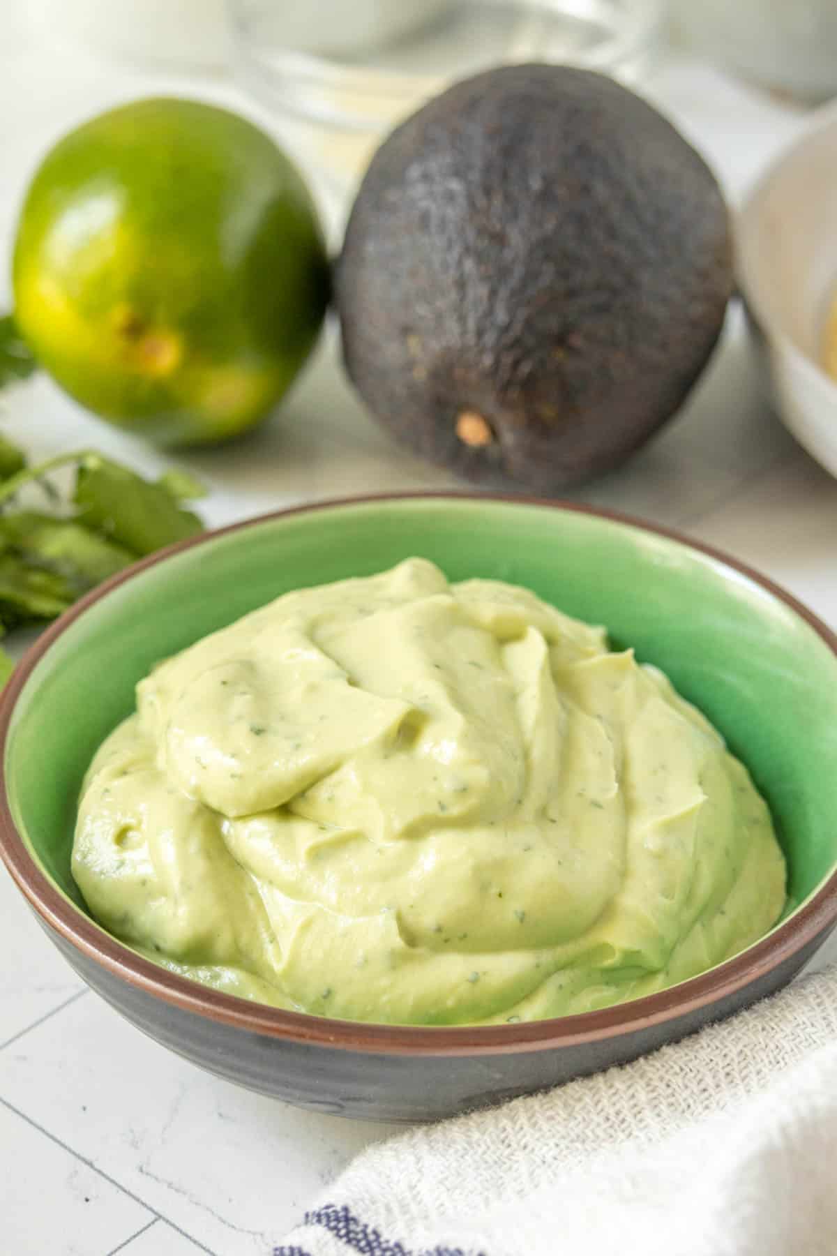 Avocado crema in a bowl with limes and other ingredients.