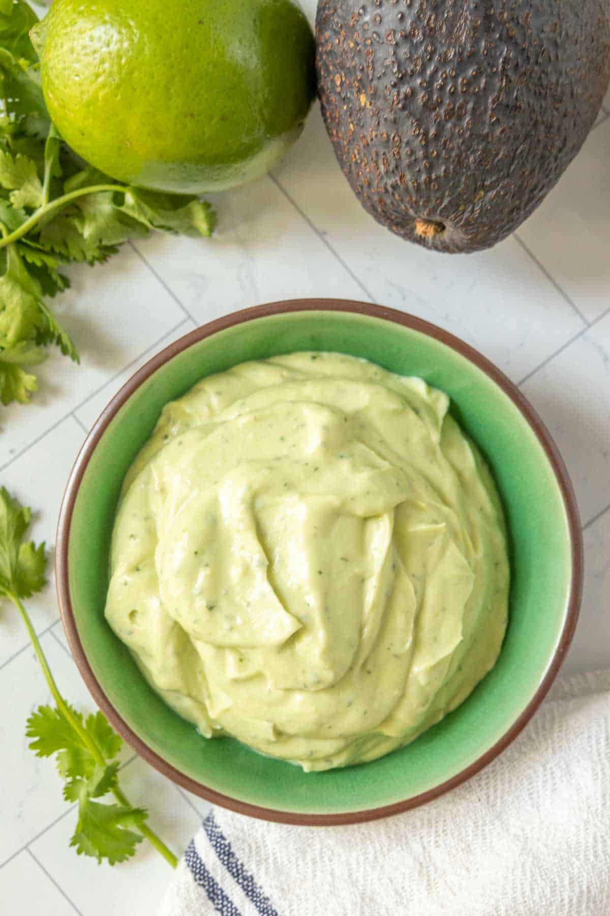 Avocado lime crema in a bowl next to a lime and avocado.