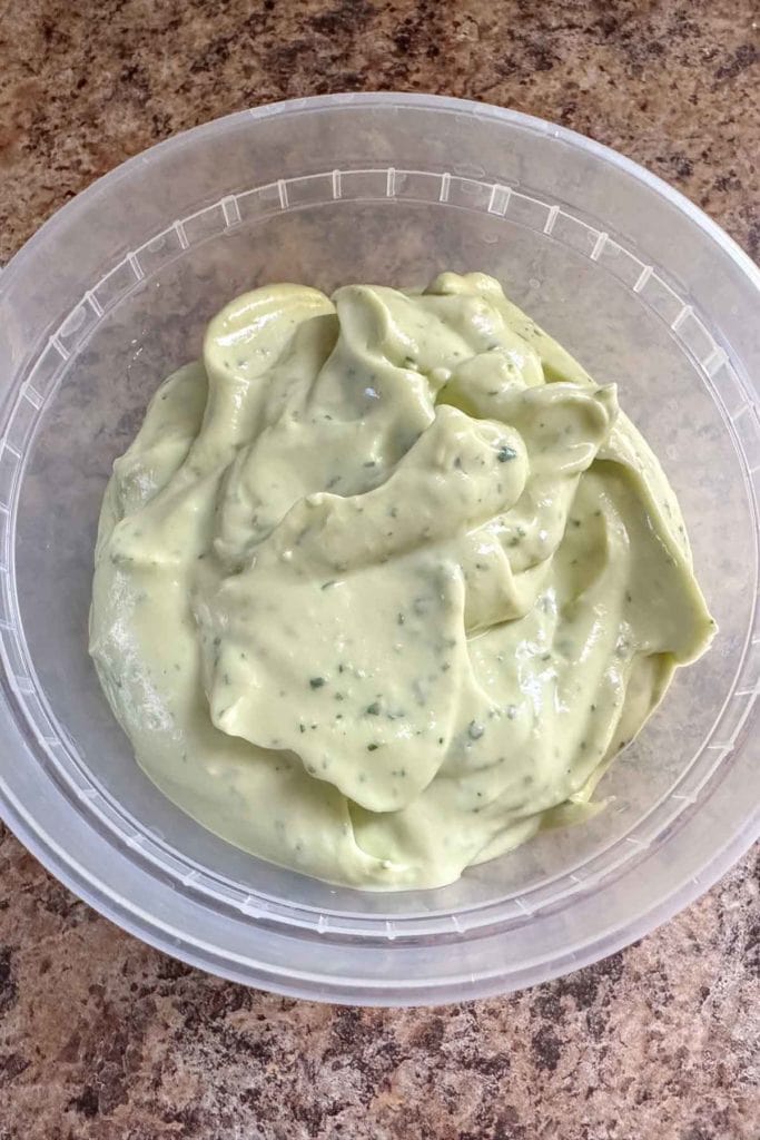 A clear plastic bowl with a green sauce in it.