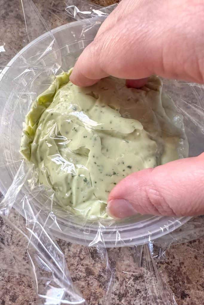 A hand is holding a plastic container with a green sauce in it.