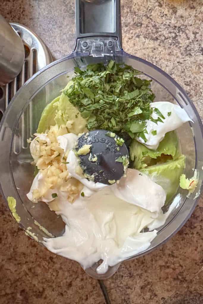 The ingredients for avocado crema in a food processor.