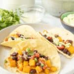 Three black bean squash tacos on a white plate.