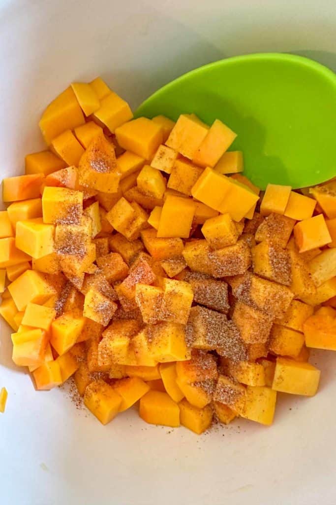 Butternut cubes in a white bowl with a green spoon.