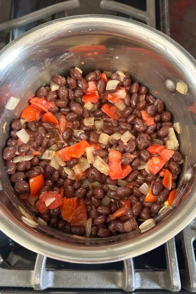 A pot with black beans, onions and peppers on the stove.
