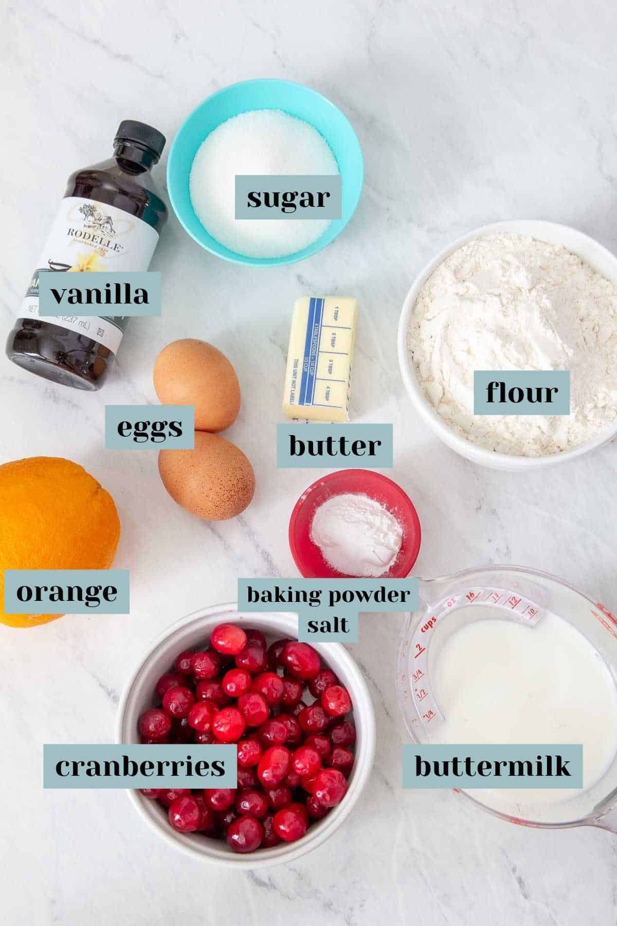 The ingredients for a cranberry orange bread on a marble countertop.