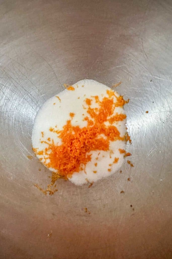 A mixing bowl with sugar and orange zest.