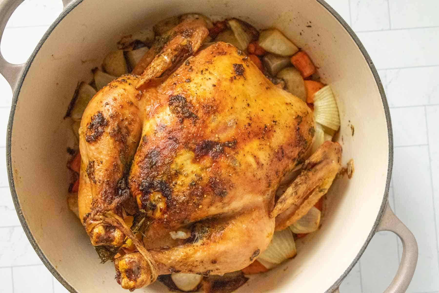 A roasted chicken in a pot with carrots and onions.