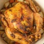 A roasted chicken in a pan with carrots and onions.