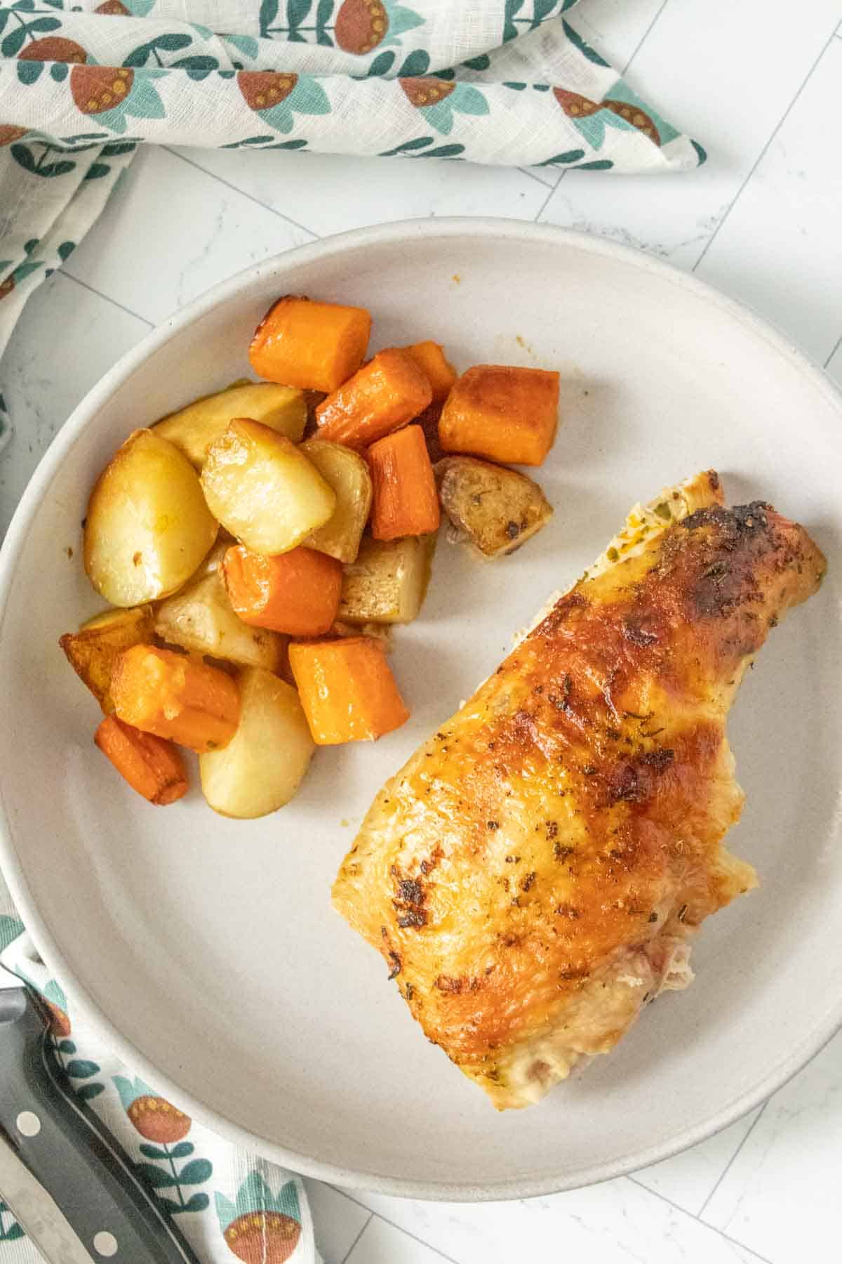 Roasted chicken with carrots and potatoes on a white plate.
