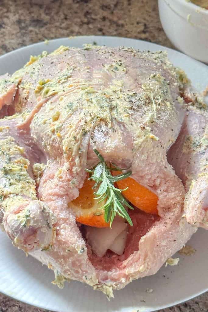 An uncooked chicken on a white plate with oranges and sprigs of rosemary.