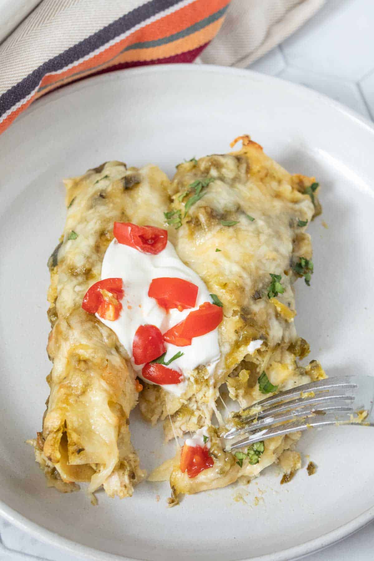 Enchiladas on a plate with sour cream and tomatoes.