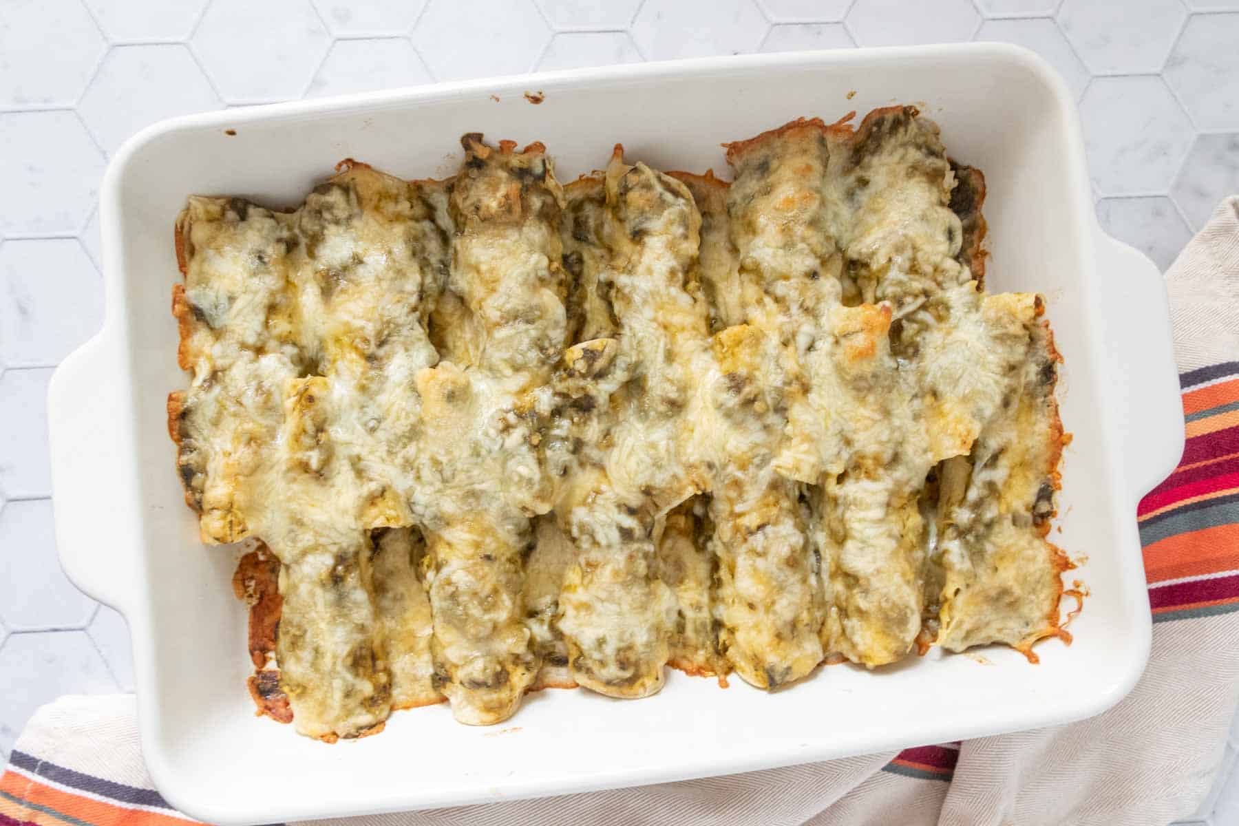 Cheesy enchiladas in a white baking dish.