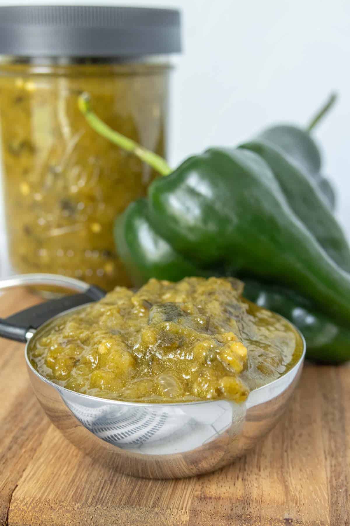 A jar of green chile sauce next to a bowl of green peppers.