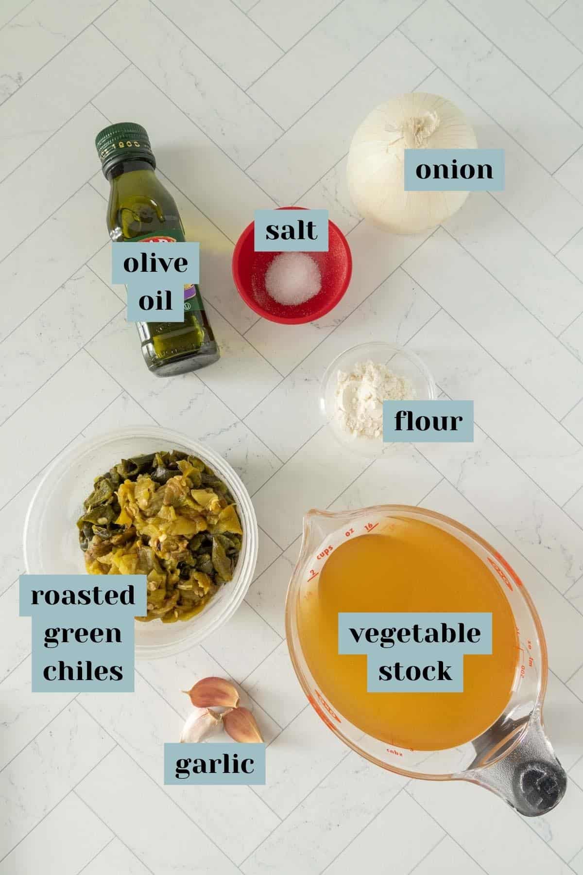 Olive oil, garlic, onion, and other ingredients are laid out on a marble countertop.