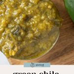 A close-up of green chile sauce in a metal measuring cup, beside a fresh green bell pepper on a wooden surface. Text reads "green chile sauce.
