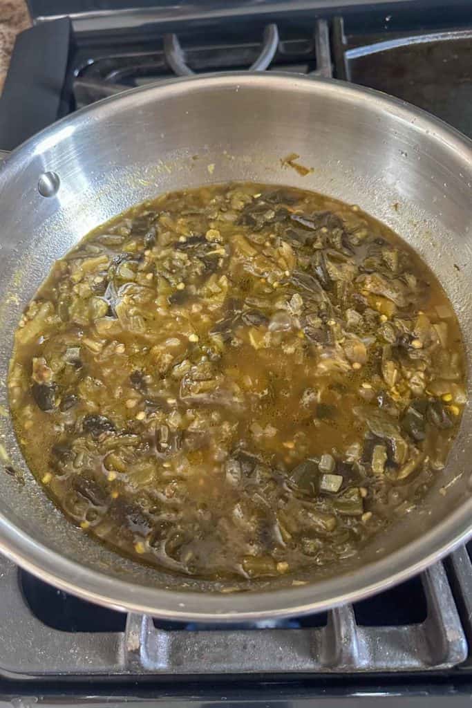 A pan full of green chile sauce on a stove top.